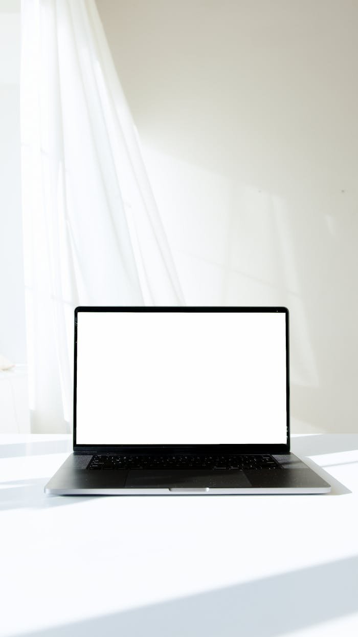 Minimalist mockup of a modern laptop with a white screen on a bright indoor surface.